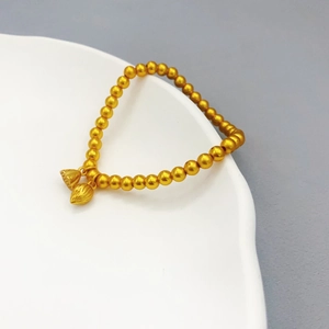 Macro di bracciale con perline d'oro opaco e ciondoli a forma di loto su piatto bianco