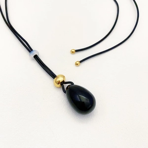 Teardrop black onyx pendant on long leather cord with gold beads shown from a 45-degree angle