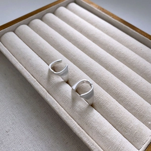 Orecchini a cerchio minimalisti a forma di U in argento opaco su cuscino beige