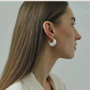 Detailed close-up of textured C-shaped metal earrings worn by a model in a minimalist style