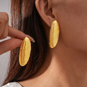 Close-up of vintage large oval gold earrings with textured spiral brushed metallic finish