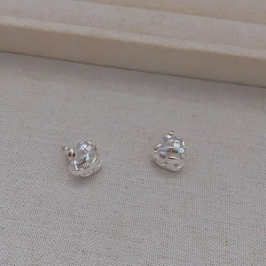 Silver woven heart stud earrings with a hollow geometric texture on a beige fabric stand