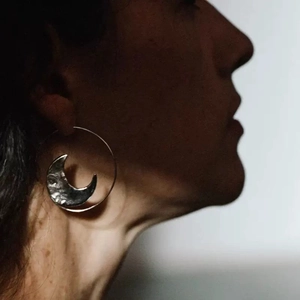 Detail of silver hoop earring with hammered texture moon pendant on female model