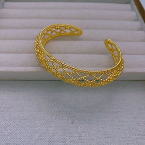 Detail of a gold-plated hollow mesh open bangle with intricate woven texture and vintage style