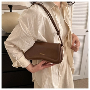 Detail of dark brown PU leather underarm bag with knot strap and golden logo text