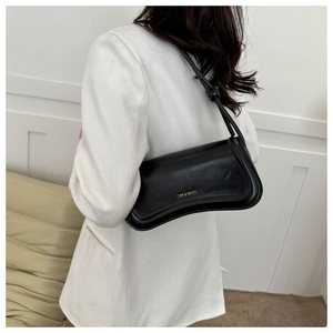 Close-up of black minimalist leather underarm bag with gold logo on a white blazer