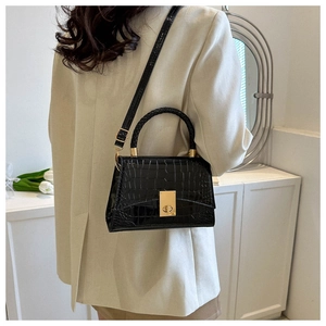 Detail of black crocodile pattern handbag with gold twist-lock and woven handle on a model