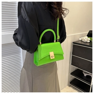 Detail of neon green crocodile texture handbag with woven handle and gold twist lock