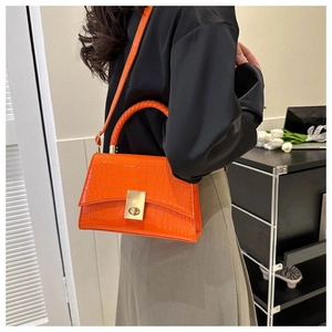 Detail of bright orange crocodile-textured handbag with a woven handle and metallic clasp