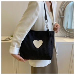 Dettaglio della borsa tote nera con patch a cuore bianco e tessuto a maglia ondulata