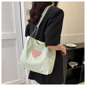 Dettaglio borsa tote in tela verde chiaro con patch cuore rosa e tracolla a catena