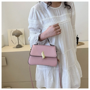 Close-up of pink trapezoid handbag with gold S-shaped buckle held by model in white lace dress