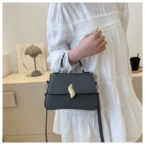 Detail of grey crossbody bag featuring a golden leaf metal lock and elegant lace outfit