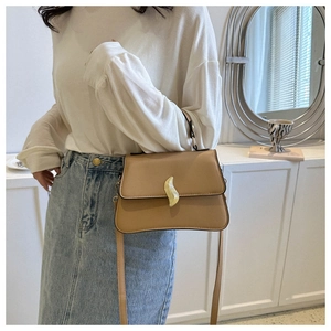 Detail of light brown crossbody bag featuring elegant gold leaf twist lock on flap