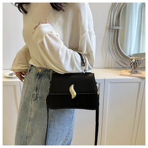 Detail of elegant black trapezoid handbag featuring a unique gold wave buckle and matte finish