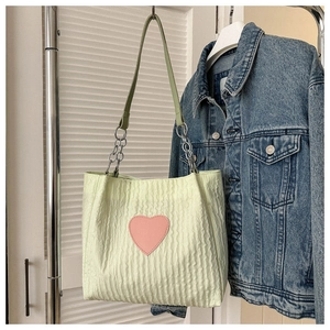 Dettaglio borsa tote verde chiaro arricciata con cuore rosa e tracolla a catena
