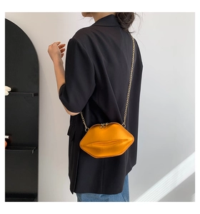Détail du sac chaîne brillant en forme de lèvres orange nacré sur un blazer noir