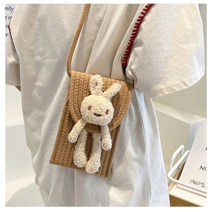 Détail d'un petit sac bandoulière tissé marron orné d'une adorable peluche de lapin