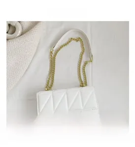 Detail of white quilted crossbody bag with golden chain strap on a soft fabric backdrop
