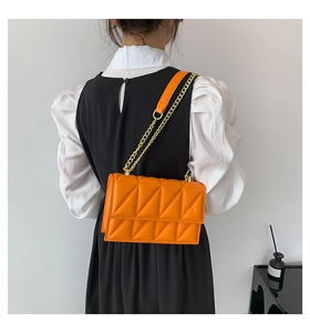 Close-up of vibrant orange quilted shoulder bag with golden chain strap on a model