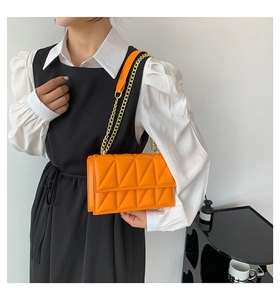 Close-up of bright orange quilted chain bag with geometric stitching and gold hardware