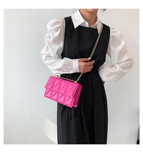Detail of fuchsia quilted crossbody bag with gold chain strap on a model outfit