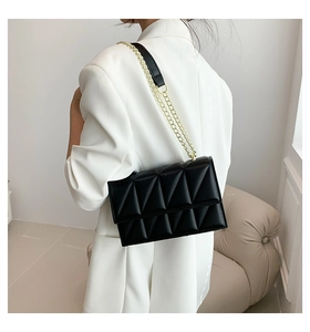 Detail view of the black quilted crossbody bag with gold chain strap on a model