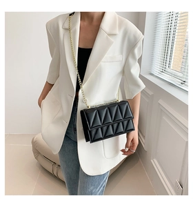 Detail of black quilted crossbody bag with gold chain strap worn by a woman in a suit