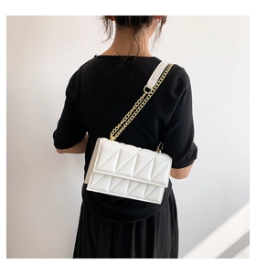 Detailed view of white quilted crossbody bag with gold chain strap on a model