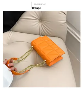 Detail of orange quilted chain bag with triangular stitching on beige leather sofa