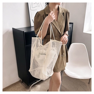 Detalle de un bolso tote de malla blanca con etiqueta tejida sostenido por una modelo