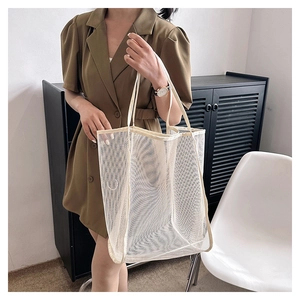 Detalle de bolsa tote de malla crema llevada por una modelo en un entorno moderno