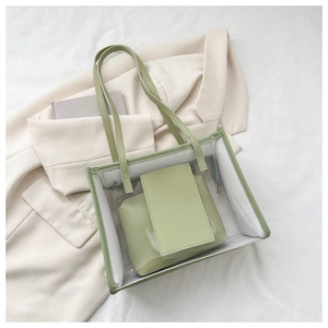 Flat lay of a transparent PVC tote bag with a sage green leather inner pouch and handles