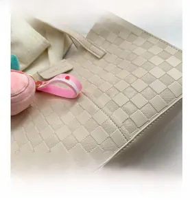Detail view of cream tote bag featuring embossed checkerboard texture and peach charm