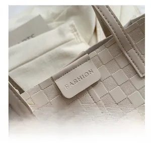 Detail of beige woven texture tote bag featuring a leather patch and gold metal hook