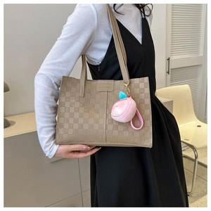 Detail of khaki tote bag with embossed checkerboard pattern and a peach plush charm