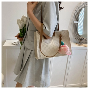 Beige plaid woven tote bag with brown leather straps and a pink peach plush pendant detail