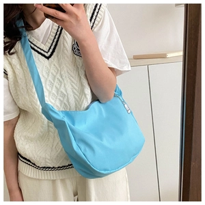 Close-up of a light blue crescent shoulder bag with wide adjustable strap and zipper