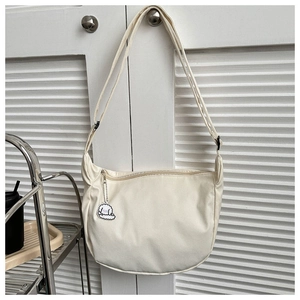 Close-up of beige nylon crescent bag with adjustable strap and cute puppy pendant