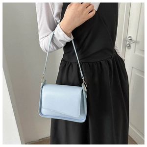 Detail of light blue trapezoid shoulder bag with gold hardware and asymmetric flap design