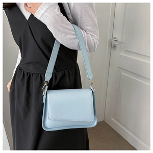 Detail of light blue minimalist leather crossbody bag with wide strap on shoulder