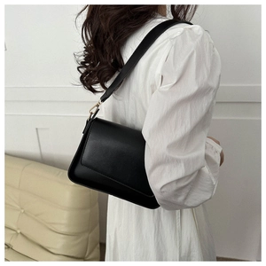 Detailed side view of a minimalist black matte leather underarm bag on a model