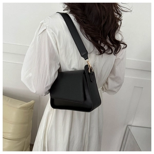 Detail of minimalist black leather crossbody bag with wide strap and gold hardware hooks