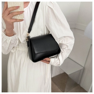 Chic black trapezoid shoulder bag with gold hardware shown on a white dress
