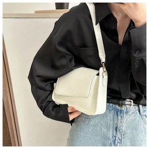 Close-up of cream rectangular flap bag with wide strap and light gold metal buckle