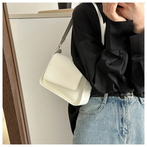 Close-up of a white minimalist flap shoulder bag worn with a black shirt and jeans