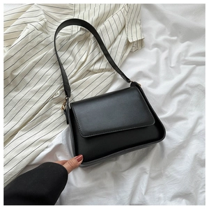 Close-up of black matte leather shoulder bag with gold metal hardware and flap closure