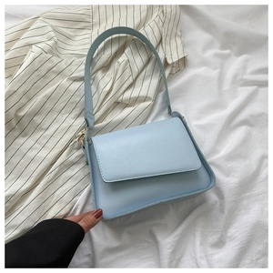 Detail view of a light blue PU leather flap shoulder bag on a soft striped fabric