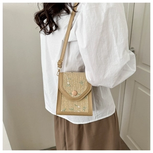 Detail of woven crossbody bag featuring green floral embroidery and tan leather strap