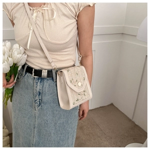 Detail of straw woven phone bag featuring floral embroidery and leather trim finish
